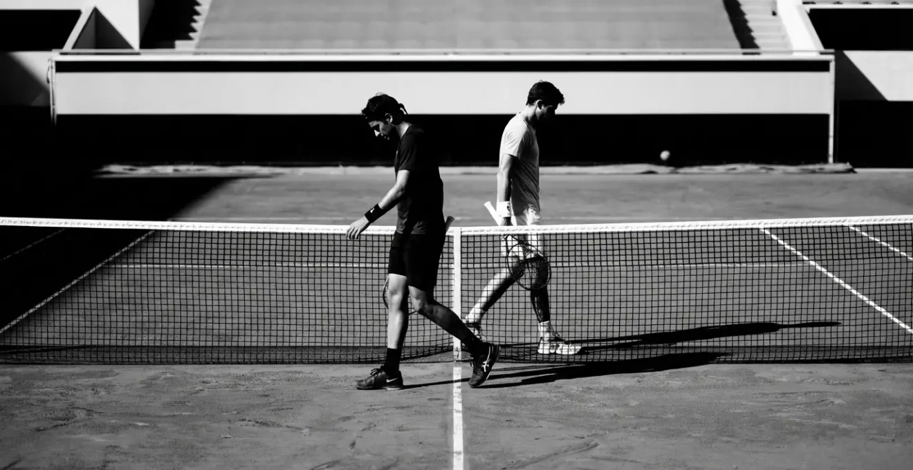 Deux joueurs de tennis se croisant au filet lors d'un changement de côté, échange de regards neutres mais intenses
