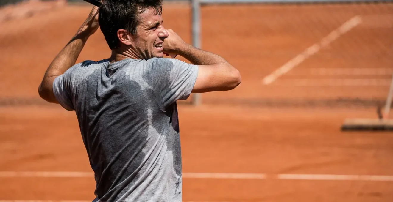 Joueur de tennis en t-shirt mouillé de sueur sur court de terre battue française sous le soleil