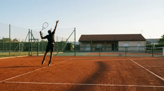 Joueur de tennis en position de service dans un club français avec des courts en terre battue